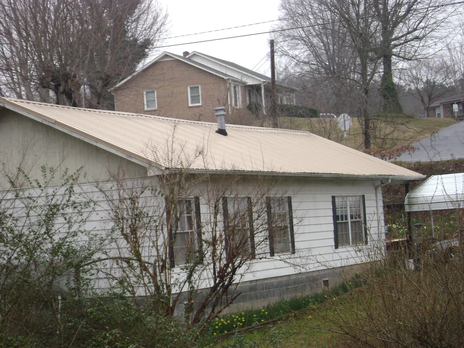 Tan metal roof on a white sided house set into a hillside — Commercial Roofing by Roofing Brothers in Glen Rock